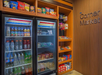 Snack and drink display at a corner market, featuring a refrigerated section with beverages and shelves stocked with chips, candies, and packaged snacks.