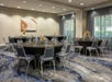 A banquet room with large round black tables set with glasses and flowers and gray tables and large windows on the far right wall.