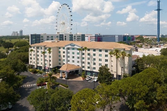 Wide shot the front exterior of the Fairfield Inn & Suites Orlando International Drive with trees around it and a ferris wheel in background.