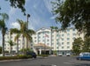View of the front exterior of the Fairfield Inn & Suites with several cars in their parking lot, tall palm trees in their landscaping and a blue sky overhead.