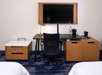 A hotel room workspace with a flat-screen TV, black desk with a chair, a lamp, a water bottle, a coffee maker, and cabinets.