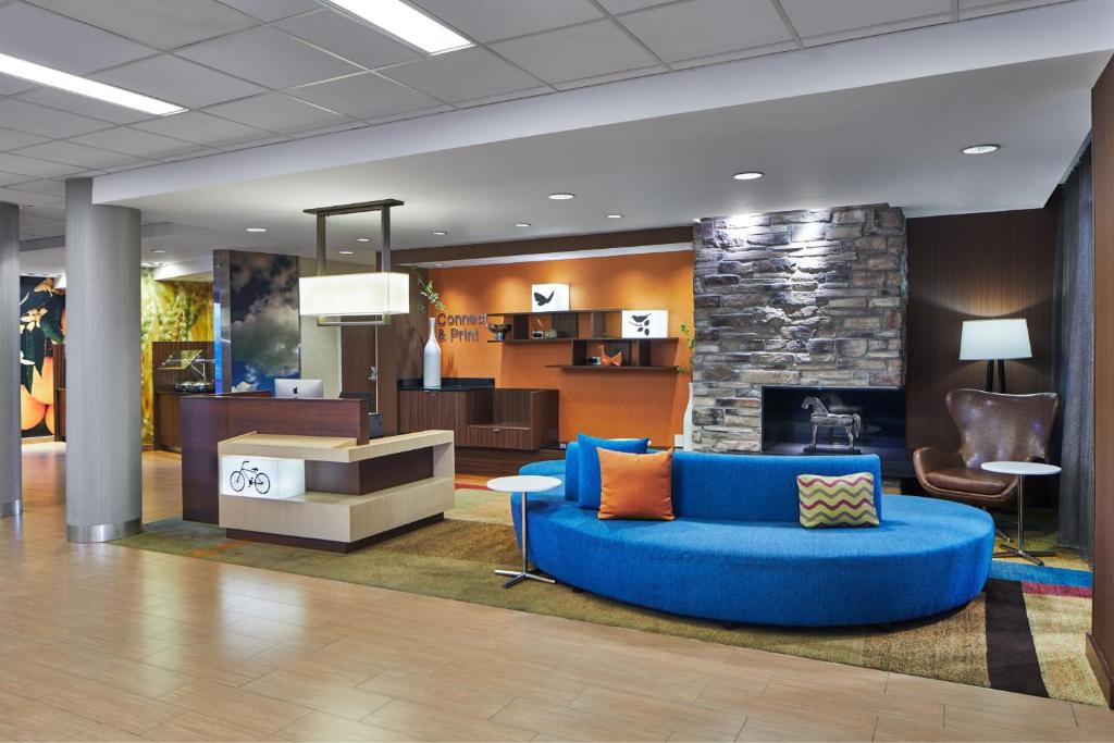 Hotel lobby with a modern design, featuring a blue circular sofa, orange and patterned pillows, a stone fireplace, a reception desk, and decorative art on the walls.