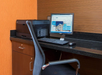 A small office workstation with a Dell desktop computer, keyboard, mouse, and printer on a black countertop against wood-paneled walls.