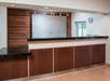 Hotel reception desk with dark wood panels, a black countertop, a clock on the wall, and a large decorative glass panel behind the desk.