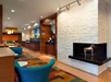 Modern hotel lobby with a white stone fireplace, decorative horse sculpture, colorful seating, and patterned carpet, with a dining area visible in the background.