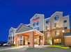 The image shows the exterior of a Fairfield by Marriott hotel at dusk, with bright lights illuminating the front entrance and parked cars visible in the lot.