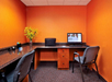 Office space with orange walls, a desk, a chair, a computer, a printer, and a vase with yellow flowers.