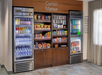 Snack and drink corner market with two refrigerators and a central shelf displaying a variety of beverages, snacks, and convenience items.