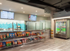 A modern snack bar with shelves of chips, a soda fridge, and a counter for ordering food; menu boards are displayed above the counter.