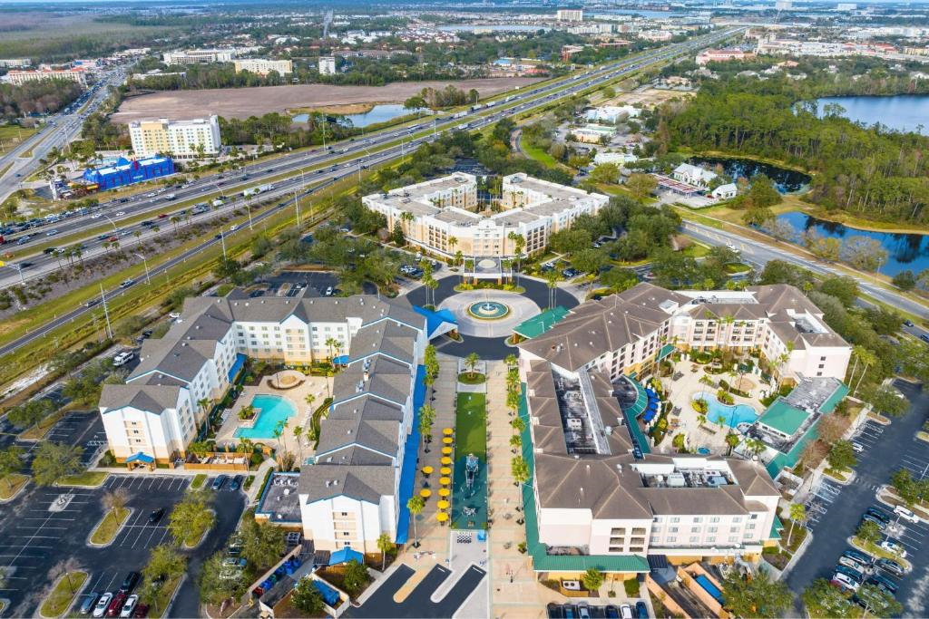 Aerial view of a hotel complex with pools, courtyards, parking lots, and surrounding roads, set near a highway and green spaces.