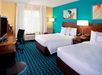 Hotel room with two double beds, teal accent wall, modern decor, desk with chair, flat-screen TV, and window with white curtains letting in natural light.