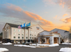 Hotel exterior with the "Fairfield Inn & Suites" sign, three flagpoles, and a snow-covered landscape under a colorful sky.