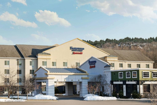 Hotel building with the sign "Fairfield Inn & Suites by Marriott" on the facade, surrounded by snow-covered grounds and trees.