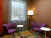 Two purple chairs and round white tables in a room with wooden walls, a floor lamp, and a window with sheer curtains.