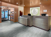 Hotel lobby with a modern design features a reception desk, illuminated artwork, and a small corner market with refrigerated beverages and snacks.