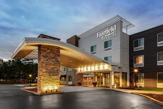 Modern hotel exterior with stone accents, large covered entrance, and illuminated signage reading "Fairfield Inn & Suites.