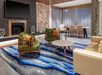 Modern lounge area with a blue abstract rug, green and beige seating, a stone accent wall, and a dining table with chairs near large windows covered by sheer curtains.