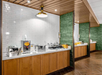 Buffet setup with serving stations along a tiled wall, featuring various containers and trays, with overhead lighting and wood-paneled decor.