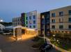 Front view of a Fairfield Inn & Suites by Marriott hotel at dusk, featuring a modern facade with illuminated entrance and surrounding parked cars.