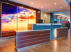 Hotel reception area with a sunset mural behind two brown counters, a blue mosaic front, and hardwood flooring. Ornamental red flowers are on one counter.