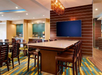 A modern meeting room with a large table surrounded by chairs, a wall-mounted TV, and contemporary lighting. The floor has a vibrant, multicolored carpet.