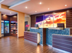 Hotel lobby with a blue-tiled reception desk, colorful sky artwork, and a corner market stocked with snacks and beverages. Two computer monitors are on the desk.