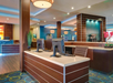 Modern hotel lobby with wooden furnishings, computer stations on the front desk, decorative art, and warm lighting.