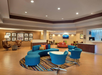 A hotel lobby with blue curved seating, a central white table, and framed art on the walls. The space includes a reception desk and warm lighting.