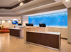 Hotel reception area with three wood-framed check-in counters and a blue abstract design wall behind. Ceiling lighting illuminates the space.