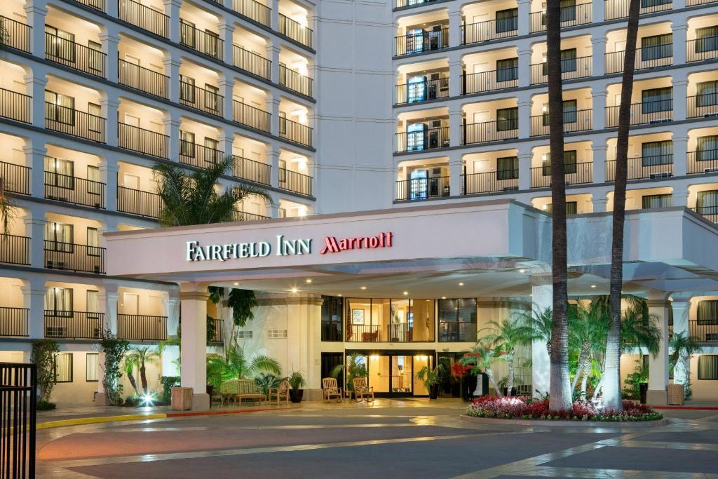 Exterior view of a multi-story Fairfield Inn by Marriott hotel, featuring balconies, illuminated windows, and a central entrance surrounded by palm trees.