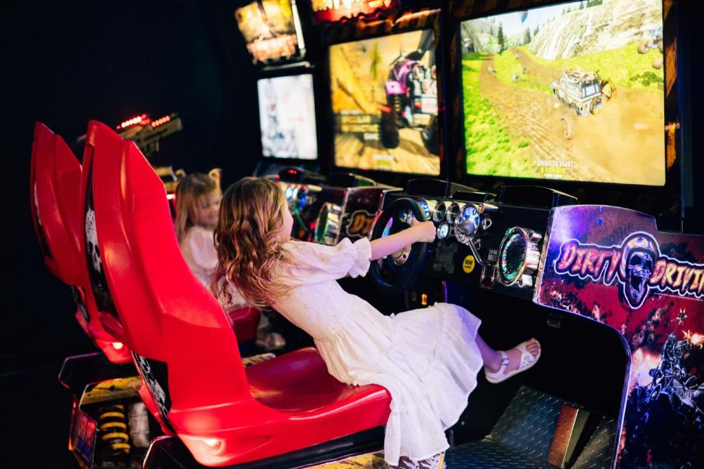Two children sitting in red seats play a racing video game at an arcade.