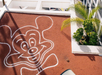 A large, stylized cartoon mouse face is drawn in white on a reddish-brown rooftop next to a green palm plant.