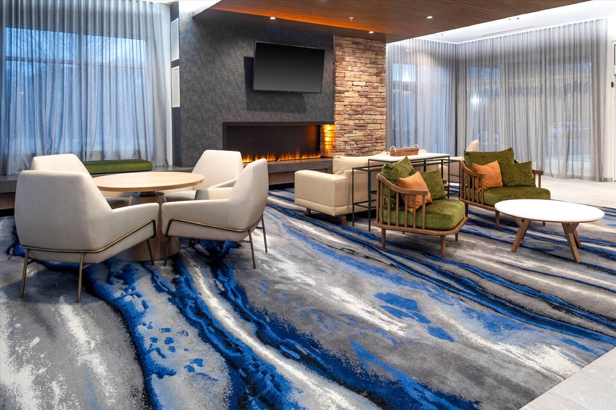 Modern lounge with abstract blue and gray carpet, stone fireplace, and seating area featuring white chairs and green cushioned sofas.