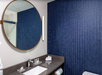 Bathroom with round mirror, dark countertop, sink, toiletries, and blue textured wall. Towels are neatly folded on the counter.