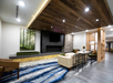 Modern lounge area with wood ceiling, stone accent wall, wall art of a forest, blue patterned rug, beige sofa, chairs, and a small table with decor.