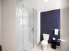 Modern bathroom with glass shower, blue textured wall, and white toilet. Towel hangs on silver bar; black trash can on floor.