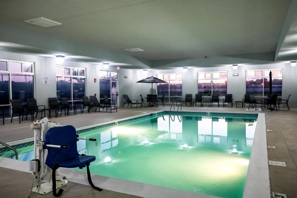 Indoor swimming pool area with surrounding chairs and tables, large windows showing a sunset view, and a pool lift on the edge.