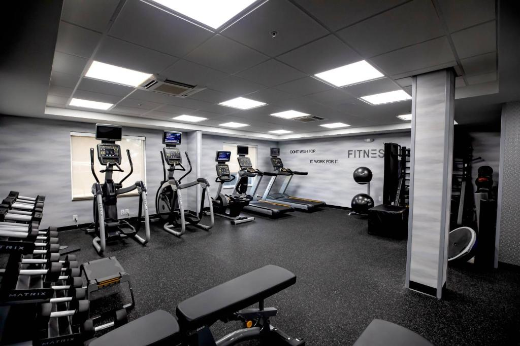 A well-lit gym with treadmills, stationary bikes, elliptical machines, dumbbells, and benches. The walls display motivational text.