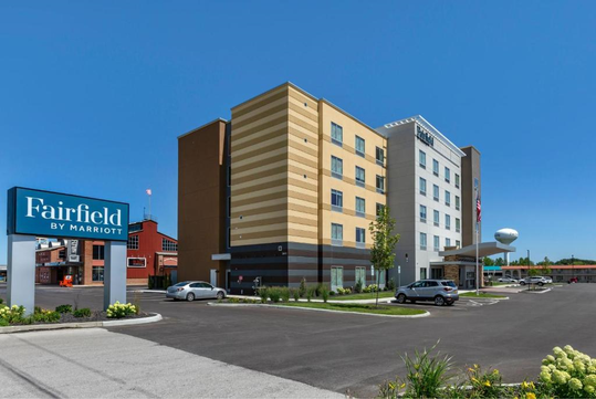 Exterior view of a Fairfield by Marriott hotel with a four-story building, parking lot, and clear blue sky.