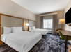 Hotel room with two double beds, a window with curtains, a floor lamp, a TV, a desk, and a chair on a patterned carpet.