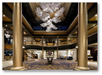 Elegant hotel lobby with grand staircase, two large columns, a central table with flowers, and a modern chandelier hanging from the ceiling.