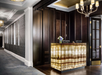 Luxurious hotel lobby with a decorative onyx reception desk, dark wood panels, a chandelier, and a patterned carpet.