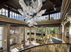 Spacious lobby with large, sculptural chandelier, tall windows, gold accents, and a sweeping staircase.