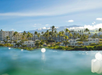 Ocean view of a coastal resort with palm trees and mountains in the background under a clear blue sky.