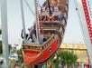 People riding a swinging pirate ship amusement park ride, with some riders raising their hands and a building visible in the background.