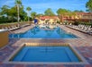 Outdoor swimming pool area with lounge chairs, palm trees, and a small hot tub in the foreground.