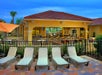 Patio with lounge chairs facing a fenced area with tables and chairs under a roofed outdoor bar.