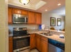 Modern kitchen with wooden cabinets, stainless steel appliances, granite countertops, a double sink, and an open view into the dining area with two framed wall art pieces.