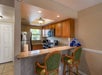 A kitchen with wooden cabinets, stainless steel appliances, granite countertops, and two green barstools at a breakfast bar. Rolled towels are stacked on the counter.