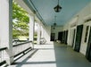 A long white front porch with black and white railing on the left with the trees in the background and windows with black shutters on the right.